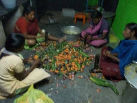 Women sitting on a stone floor preparing ingredients for a meal.