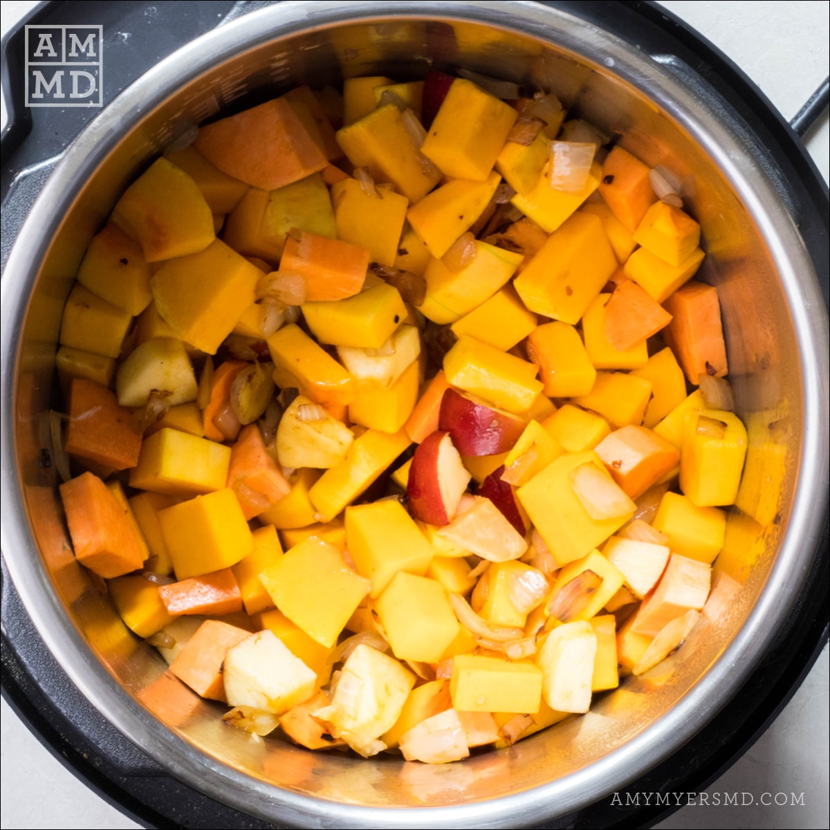 An immersion blender filled with fresh chunks of sweet potato, apples, and butternut squash