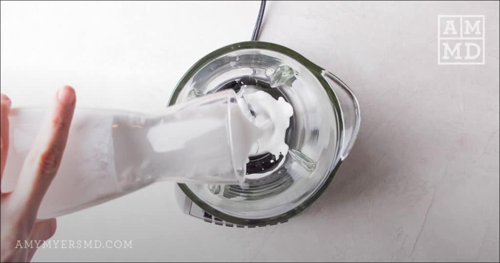 Full-fat coconut milk being gently poured into a blender to make a healthy tropical smoothie