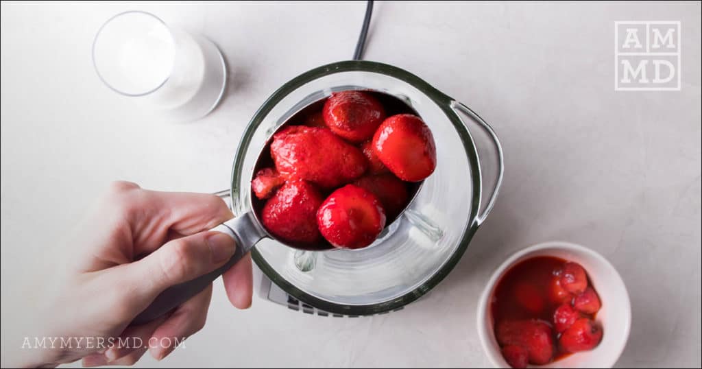 Half a cup of frozen strawberries being added to a blender to make a tropical strawberry mango smoothie