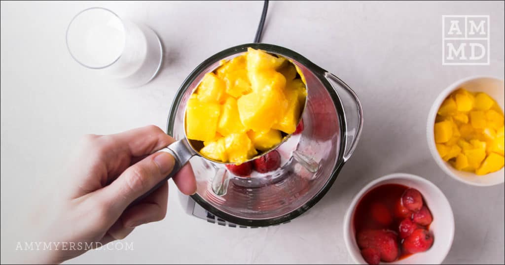 Half a cup of frozen mangos added to a blender filled with coconut milk and frozen strawberries