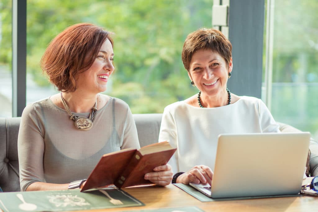 Two women having a conversation in a coffee shop together, smiling.
