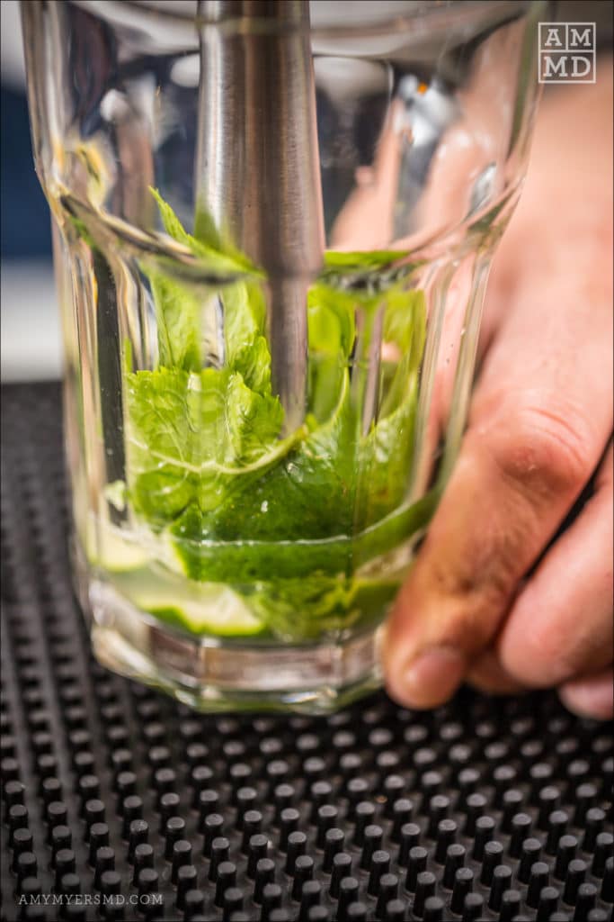 Mint leaves being crushed in a glass for making an AIP-friendly watermelon mint drink