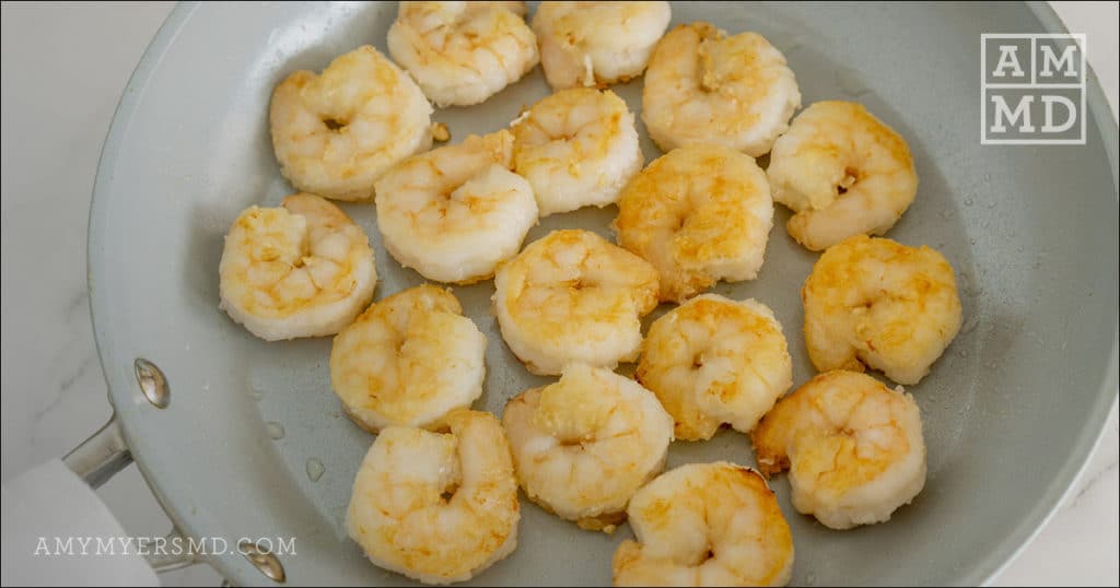 AIP-friendly bang bang shrimp sizzling in a pan coated with fresh grated garlic, sea salt, and black pepper