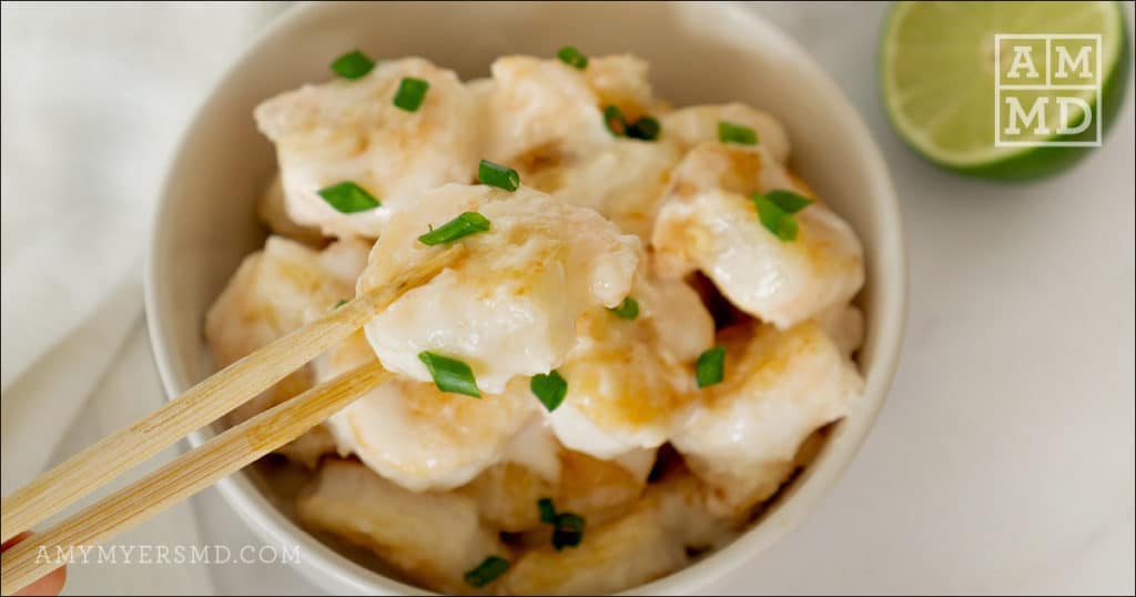 A piece of AIP-friendly bang bang shrimp being picked up gently with wooden chopsticks