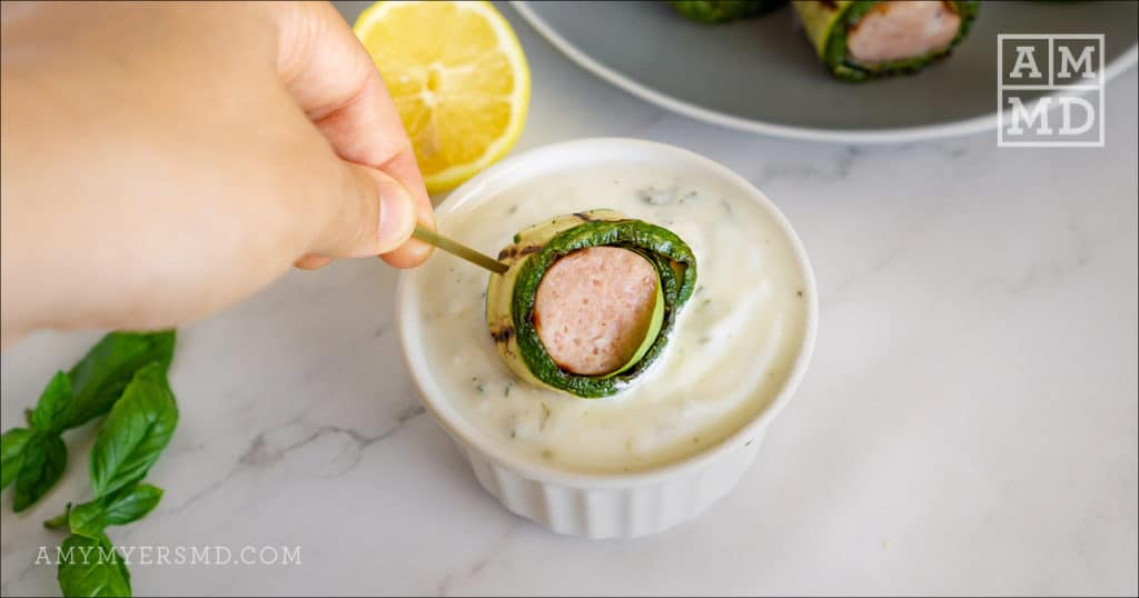 Dipping a zucchini-wrapped sausage bite into the creamy dip