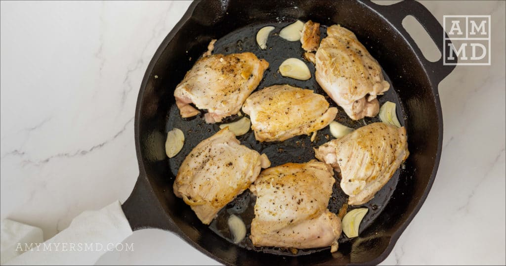 Several chicken thighs seasoned with Mediterranean spices simmering in a cast iron skillet